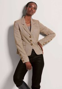 Bruine tweed blazer met gouden knopen, met notch-revers en twee voorkruiszakken, gecombineerd met een slank zwart broek. Gladde textuur en op maat gemaakte pasvorm.