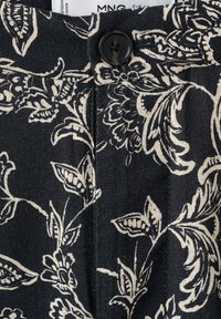 Tissu à motif floral noir et blanc avec un bouton noir et un pli cousu près de la ceinture.