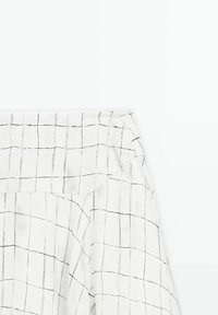 Tissu blanc avec un motif à grille noire comportant des lignes verticales et horizontales irrégulières, dessinées à la main, montrant une section pliée.