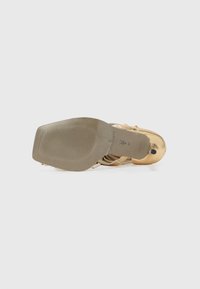 Gold strappy high-heeled sandal featuring a smooth metallic finish, a curved heel, and a textured rubber sole with a central logo.