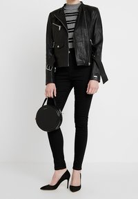 Sort lædermotorcykeljakke med sølv hardware, stribet top, sorte skinny jeans, cirkulær sort håndtaske og sorte højhælede sko.