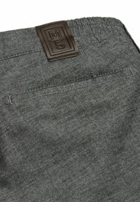 Rückansicht von grauen Stoffhosen mit elastischem Bund, einer eingearbeiteten Tasche und einem braunen Lederpatch mit der Aufschrift "M5" in der Nähe des Bundes.