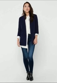 Marineblazer, lange ermer, kombinert med en hvit skjorte og mørkeblå skinny jeans. Svarte ankelstøvler og glatt stofffinish.