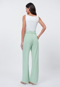 Light green, wide-leg pants with a high waist and back pockets. Paired with a fitted white sleeveless top. Smooth fabric texture.
