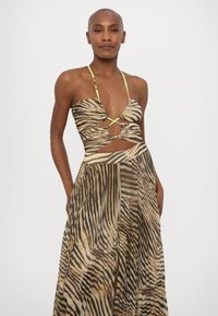 Abito senza spalline in stampa animale beige e nera con un busto attorcigliato, dettagli con ritagli e spalline verde neon. Tessuto fluido e texturizzato.