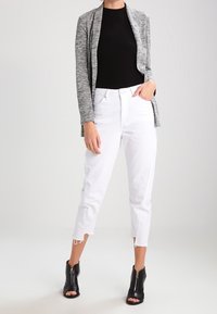 Šedý melírovaný kardigan, černý žebrovaný top a bílé zkrácené džínsy s neupraveným lemem, doplněné černými otevřenými kotníkovými botami.