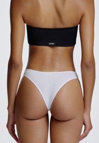 Haut bandeau noir et tanga blanc, tous deux en tissu doux. Le bandeau comporte un petit logo métallique à l'arrière.