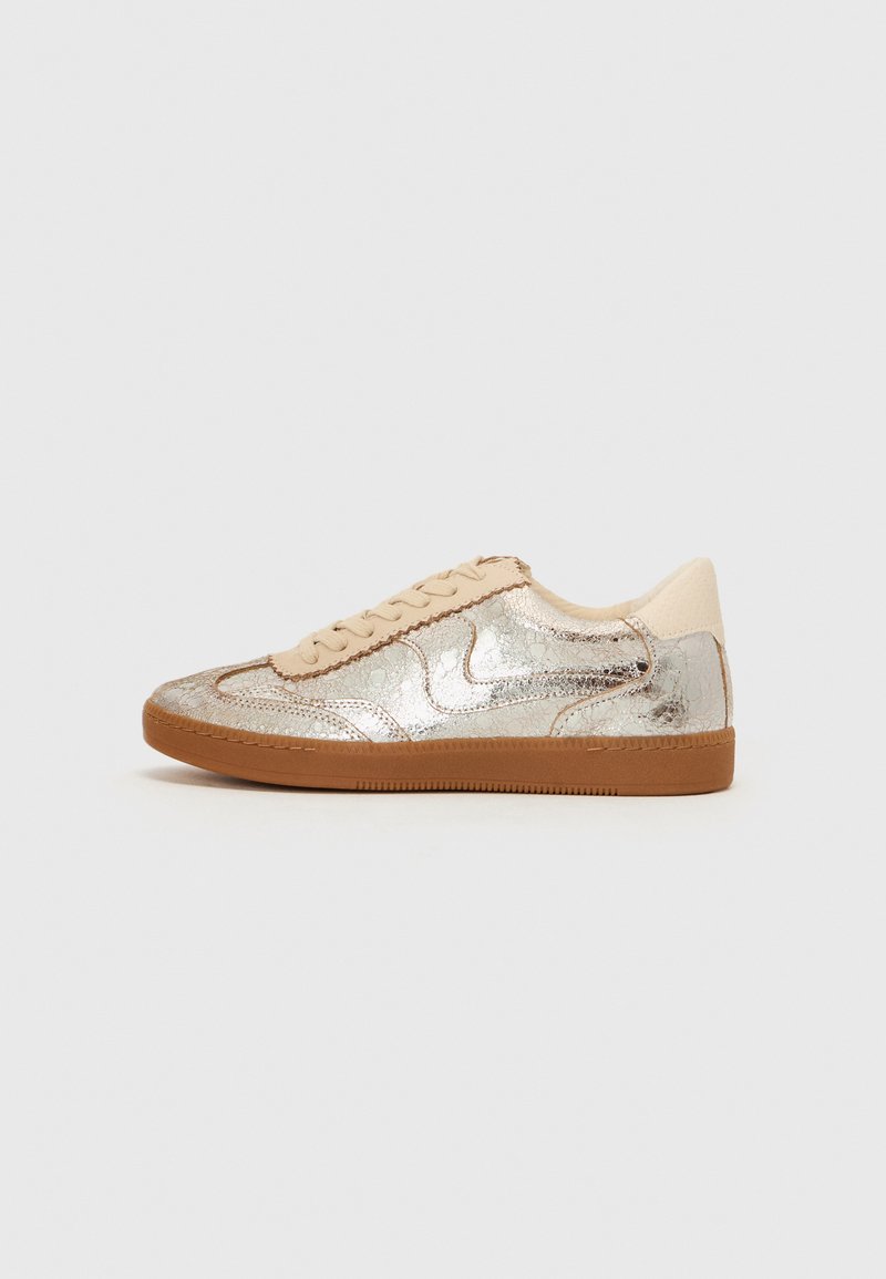 Silver metallic sneaker with a textured surface, beige accents, cream laces, and a brown rubber sole. Classic low-top design.