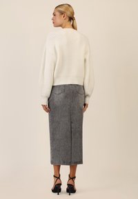 Maglione bianco lavorato a maglia con maniche a sbuffo, abbinato a una gonna in denim grigia con un motivo delicato e uno spacco sul retro. Sandali neri con tacco completano il look.