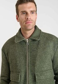 Chaqueta de lana verde con cierre de cremallera en la parte delantera, cuello puntiagudo, bolsillos de parche y un acabado texturizado. Diseño casual con una silueta estructurada.
