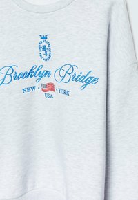 Grijze sweatshirt met ronde hals, voorzien van blauwe geborduurde tekst "Brooklyn Bridge" en een klein ontwerp van de Amerikaanse vlag. Zachte stof textuur.