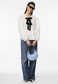 Chemisier blanc avec un détail nœud noir, manches ballons, associé à un jean en denim taille haute et un sac à main en cuir croco bleu clair.