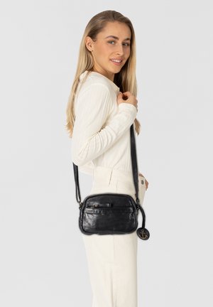 Borsa a spalla nera in pelle con finitura liscia, forma rettangolare e lungo manico. Presenta una tasca frontale con zip e un charm decorativo a forma di ancora.