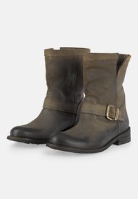 Botas de tobillo de cuero marrón con un acabado ligeramente texturizado, adornadas con una correa y detalle de hebilla, punta redondeada y tacón bajo apilado.