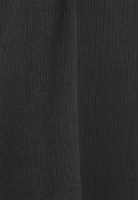 Černá tkanina s jemnou vertikální ribbovanou strukturou a mírnými záhyby, které vytvářejí měkké stíny a hloubku.