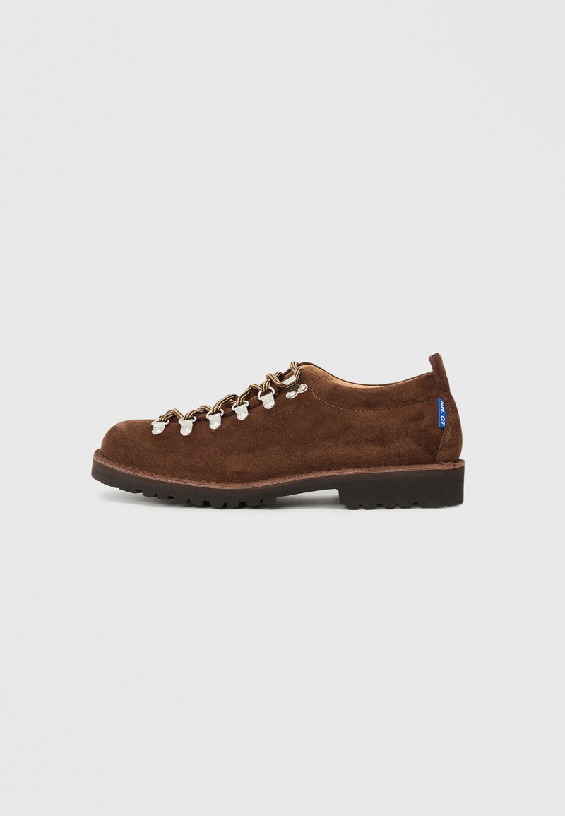 Brown suede shoes with a low-profile design, featuring metal eyelets and white laces, reinforced toe, and a textured black rubber sole.