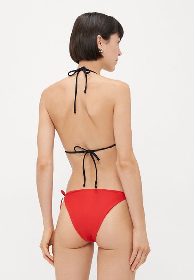 Červený bikiny so zaväzovaním na krku, čiernym uzáverom a zodpovedajúcimi bokovými nohavičkami na zaväzovanie. Hladká textúra s minimálnym zakrytím.