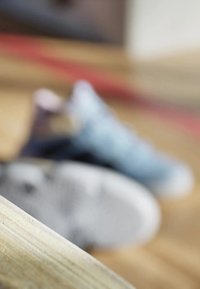 Sneakers in delicati tonalità di blu e grigio, con materiale in rete e suole testurizzate, parzialmente oscurati, su una superficie di legno in primo piano.