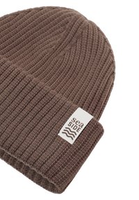 Bonnet en tricot marron avec une texture côtelée et un revers retourné. Comprend une étiquette blanche avec l'inscription "sea SIDE" et un motif de vague.