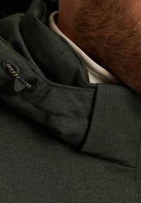Green hooded jacket featuring a textured fabric, adjustable drawstring detail, and a layered collar design. Smooth interior visible.