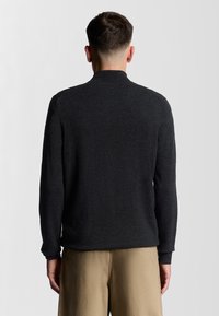 Mörkgrå långärmad tröja med hög krage, texturerad tyg och avslappnad passform. Slät yta utan synliga mönster eller detaljer.