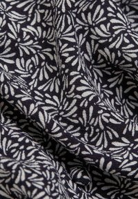 Baumwollstoff mit einem marineblauen Hintergrund, der weiße abstrakte Blattformen zeigt. Die Textur wirkt weich und leicht strukturiert.