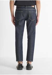 Donkerblauwe denim jeans met een slim fit, zichtbare stikseldetails, twee achterzakken en een lichte tapering bij de enkels.