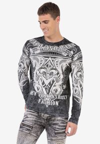 Schwarzes Langarmshirt mit weißem Grafikdesign, das Schlangen und Text zeigt, aus weichem Material gefertigt. Getragen mit lässigen grauen Jeans.