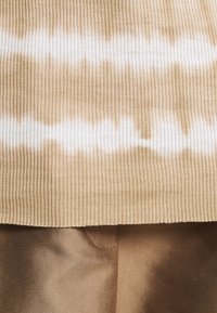 Beige žebrovaná látka s vlnitým bílým tie-dye vzorem je zobrazena spolu s hladkým saténem v mírně tmavší béžové.