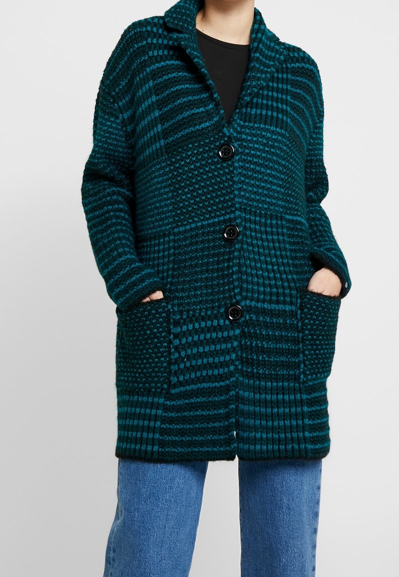 Türkis gestrickte Strickjacke mit lockerer Passform, strukturierten Mustern, einem Schalkragen, drei Knöpfen und zwei vorderen Taschen.