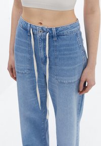 Ljusblå, högmidjade jeans som har en avslappnad passform, framfickor och midja med dragsnöre med en elfenbensfärgad knytning.