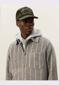 Gray wool shirt jacket with cream stripes, featuring a chest pocket and button closure. Underneath, a gray hooded sweatshirt is visible.