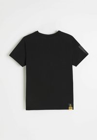 Czarny t-shirt z krótkim rękawem i okrągłym dekoltem, wykonany z miękkiej tkaniny. Posiada małą żółtą metkę z logo na dole oraz przezroczysty detal na ramieniu.