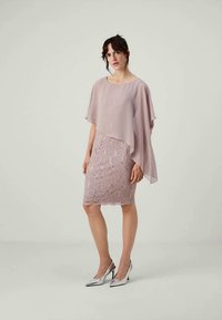 Kurzes Kleid aus hellpinkem Spitze mit Blumenmustern, schichtiger Chiffon-Cape und silbernen High Heels. Glatte Textur und taillierte Silhouette.