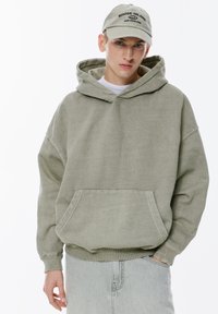Hanorac oversized de culoare verde deschis, realizat din bumbac, cu un buzunar frontal și manșete ribbate, asortat cu o șapcă cu broderie "Rhode Island."