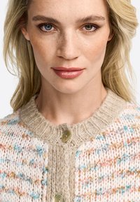 Gilet en tricot de couleur crème avec des éclats multicolores, un col texturé beige et une fermeture à bouton. Fil léger avec un tissage lâche.