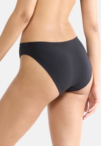 Svarta kvinnors trosor med en slät yta, högskurna benslut och ett logoband i midjan, som visar en sömlös design för komfort.