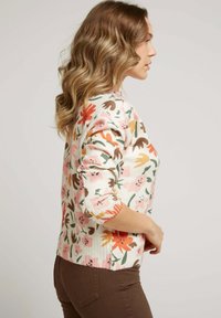 Pull floral à manches trois-quarts, avec un fond rose doux et des motifs de fleurs multicolores. Ourlet et poignets côtelés.