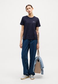Marinblå bomullströja, avslappnad passform med korta ärmar och rundad halsringning. Kombinerad med vida denimjeans och metallic silverfärgade sneakers.