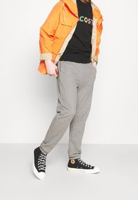 Orange vattentät jacka med beige foder, svart t-shirt med färgat logotyp, gråa mjukisbyxor och svarta högklackade sneakers med vita sulor.