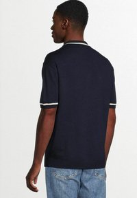 Marineblauw poloshirt met korte mouwen, voorzien van witte gestreepte accenten op de boorden en de kraag. Gemaakt van gestructureerde stof, passend ontwerp.