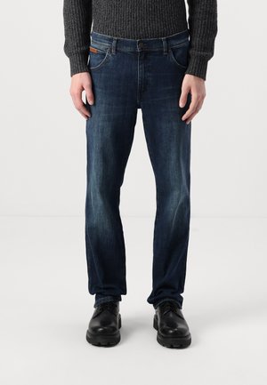 Mörkblå denimjeans med rak passform, med framfickor, kontrasterande sömmar och en brun läderlapp nära midjan.