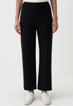 Zwarte, wijde broek van zacht materiaal, met een elastische tailleband en rechte snit. Gecombineerd met witte sneakers.