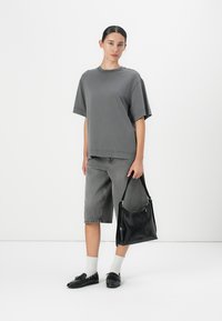Grijze oversized t-shirt, grijze denim bermuda shorts, zwarte platte schoenen, witte sokken en een zwarte leren handtas met een schouderriem.