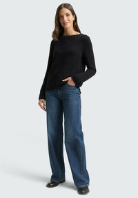 Black textured knit sweater with wide boat neckline, paired with loose-fitting blue jeans and black ankle boots. Casual outfit.