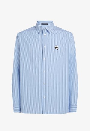 Camisa de rayas azules y blancas con mangas largas, cuello abotonado y logo en el pecho. Hecha de tela ligera con una textura suave.