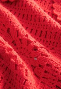 Tissu tricoté rouge présentant un motif en crochet ajouré avec des textures surélevées et des designs de points variés tout au long.