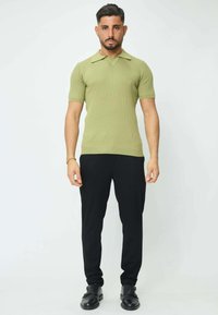 Polo à manches courtes en matériau côtelé vert clair, associé à un pantalon noir et des chaussures noires. Design de col simple ; forme ajustée et élancée.