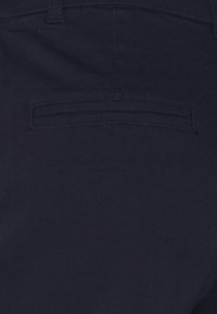 Granatowy materiał, z tylną kieszenią z subtelnym szwem wykończonym detalem. Materiał wydaje się gładki i lekko teksturowany.