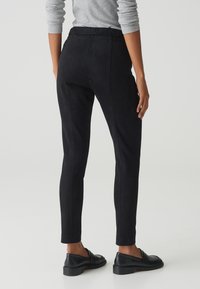 Pantalons noirs fuselés en tissu doux et mat, avec une taille plate et des coutures latérales. Associés à des mocassins noirs pour un look complet.